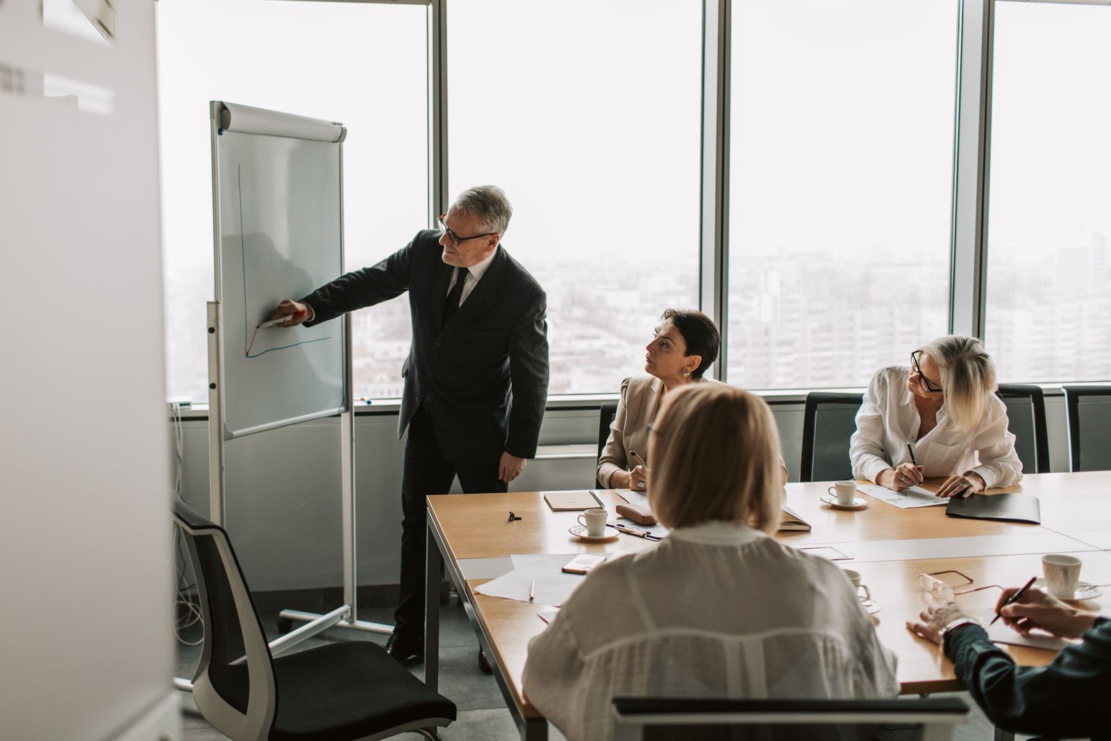 A grey-haired man drawing on a whiteboard for his team